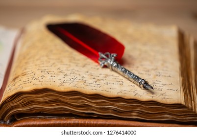 A red and silver quill pen on a hand written book on a wooden table. - Shutterstock ID 1276414000