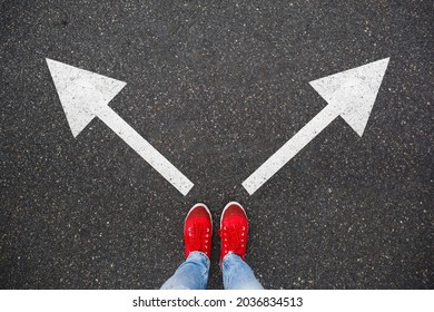 Red Sneakers On The Asphalt Road With Drawn Arrows Pointing To Two Directions. Making Decisions And Making Choices, Dilemmas Concept