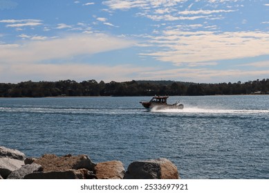 A red speedboat cruising on a lake with forested hills in the background under a partly cloudy sky. - Powered by Shutterstock