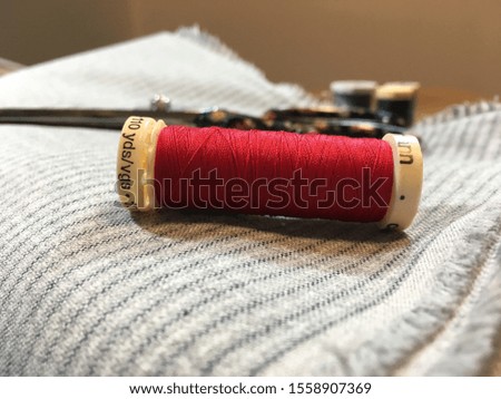 Red spool of thread on striped grey fabric. Cloth and tools ready for sewing project. Garment construction. Project readiness. 