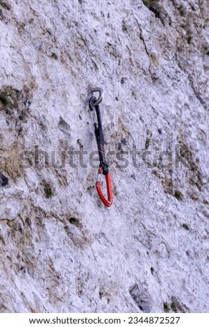 a red sport climbing quickdraw clipped in a bolt on limestone rock