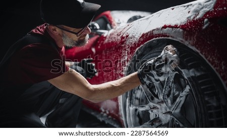 Red Sportscar's Wheels Covered in Shampoo Being Rubbed by a Soft Sponge at a Stylish Dealership Car Wash. Performance Vehicle Being Washed in a Detailing Studio