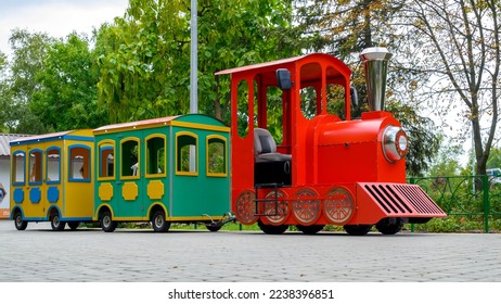 red steam locomotive with wagons, a children's attraction in an amusement park close-up against the background of green trees