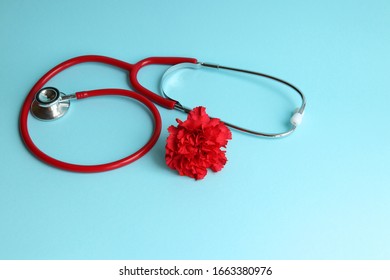 A Red Stethoscope On A Blue Background And A Red Carnation Symbolize The National Day Of The Doctor