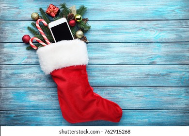 Red stocking with fir-tree branches and smartphone on wooden table - Powered by Shutterstock