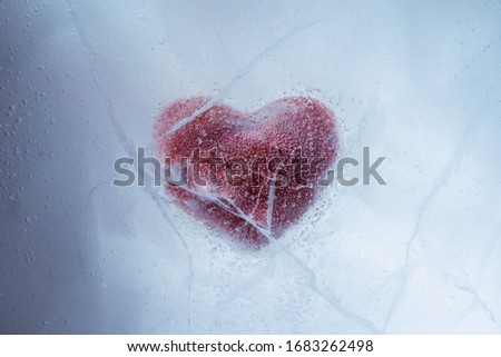 Red stone heart frozen in ice with a big cracks, a symbol of love or betrayal or separation.