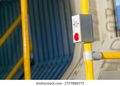 Red stop button mounted on a yellow pole inside a bus or tram with seats and windows visible in the background.