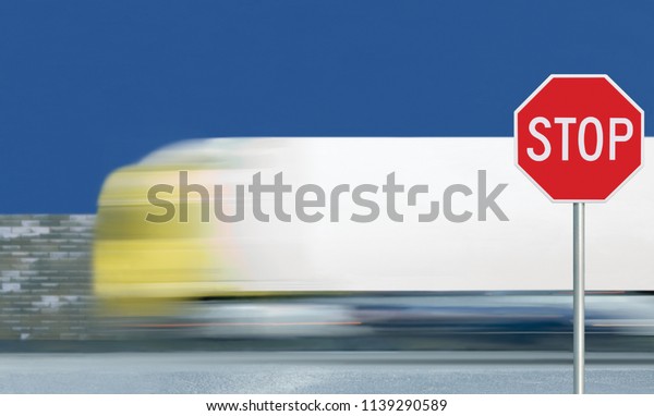 Red stop road sign,\
motion blurred truck vehicle traffic background. Give way\
regulatory warning signage octagon. White octagonal frame metallic\
pole post blue summer sky