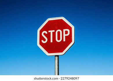 A red stop sign with texture and high contrast and a clear blue sky in the background