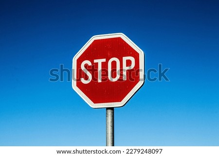 A red stop sign with texture and high contrast and a clear blue sky in the background