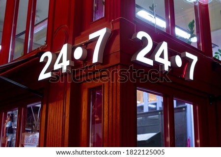 red store on the corner with a luminous sign 24/7, English style red store with glass windows, a night scene of building facade lighting details.