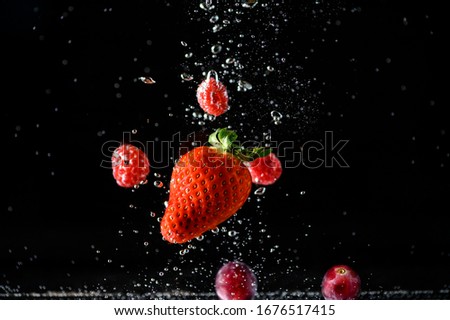 Red strawberries falling into water on black background. Fresh fruits splashing