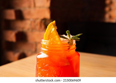 Red Strawberry Lemonade Cocktail With Soda, Ice, Orange Slice And Mint Leaf In Glass On Wooden Table. Bar Or Cafe. Closeup Of Top Of Glass, Front View.