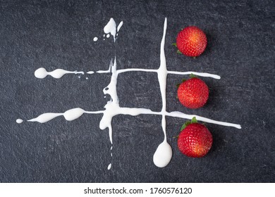 Red strawberry on a dark stone board with white sour cream. Game of tic tac toe with fresh berries.