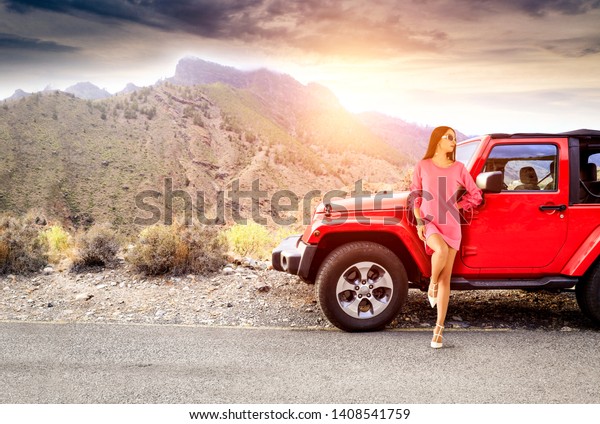 Red summer car on road trip and slim young woman\
in summer dress. Free space for your decoration and summer sunset\
time. Gran Canaria island. 
