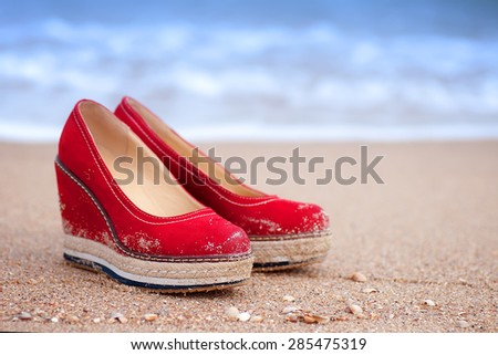 red summer shoes standing on sandy ocean beach