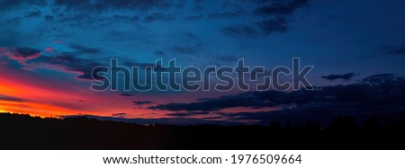 Red sunny sunset with thunderclouds on the horizon. Sky with clouds. Sunny sunset. Cloudy horizon. Forest in the dark. Evening twilight. Night time. Weather. Natural landscape. Panoramic photo.