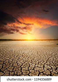 red sunset in dramatic clouds over drought earth
