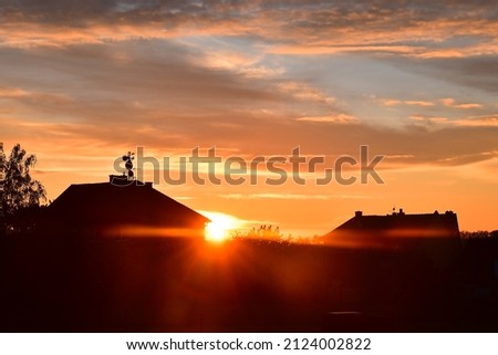 Red sunset sky clouds in countryside landscape with house roofing in a village with sun setting down evening nature view 