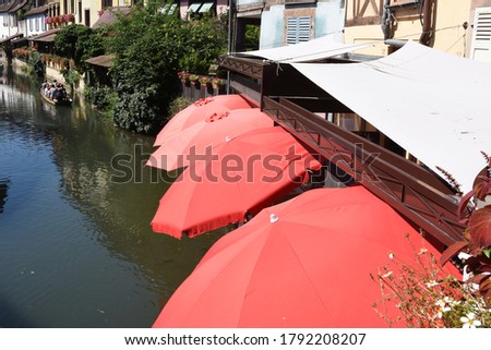 Red sunshade umbrellas along the romantic canal ,little Venice, the course of the Lauch in Colmar., with half-timbered houses along the riverbanks in north-eastern France.