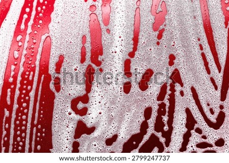 Red surface covered with soap foam and water bubbles. Car wash cleaning background. Abstract texture created during vehicle washing process with detergent and rinsing water.