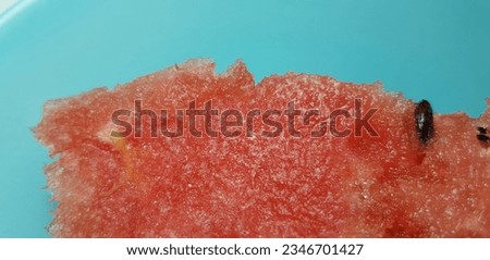 Red surface of a freshly cut slice of watermelon (Citrullus lanatus) with tiny dark seeds on a turquoise background (macro, top view, texture).