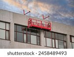 Red suspended scaffolding platform on facade of building under renovation. Plastering works at height, high-altitude plaster works on facade. Building renovation. Mobile scaffolding platform 