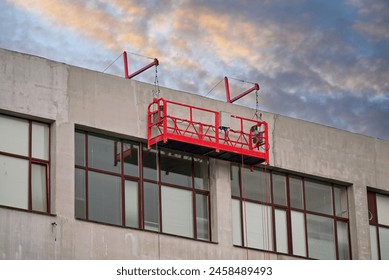 Red suspended scaffolding platform on facade of building under renovation. Plastering works at height, high-altitude plaster works on facade. Building renovation. Mobile scaffolding platform 