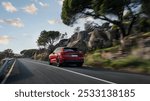 A red SUV driving swiftly along a scenic mountain road lined with rocky terrain and lush trees under a bright, partly cloudy sky