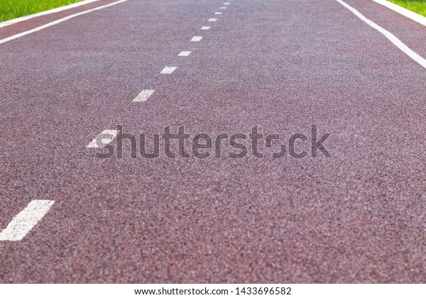 Red synthetic\
treadmill or bike lane with white markings, look straight along one\
of the lanes. Selective\
focus.