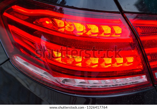 Red tail lights (rear lights, brake lights) of\
black car close up image.
