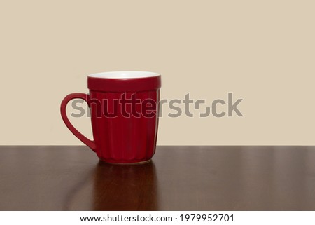 Red tall coffee mug on a brown table with a tan background
