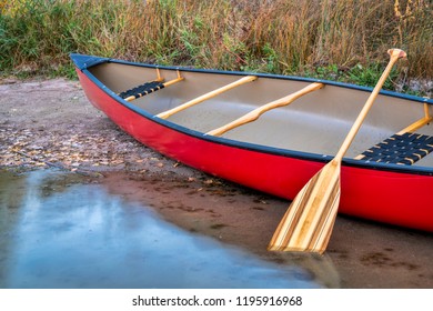 Red Tandem Canoe With A Wooden Paddle On A Lake Shore