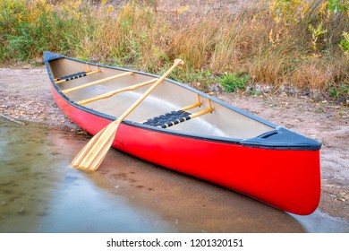 Red Tandem Canoe With A Wooden Paddle On A Lake Shore