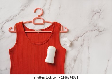 Red Tank Top On A Hanger And Solid Antiperspirant Over Marble Background. Deodorant Stick On A Linen Jersey Tank Shirt. Prevent Body Odour, Body Care, Toiletries Concept. Copy Space. Top View.