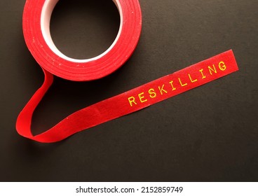 Red Tape On Black Background With Text RESKILLING, Means Learning New Skills To Do Different Job, Employees Reskilling To Move Onto New Role Within Current Company