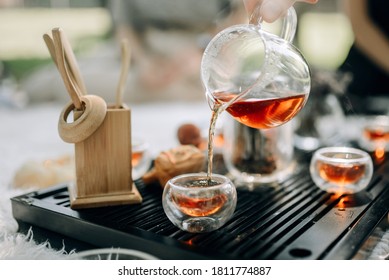 Red tea in a glass teapot is poured into cups. Tea ceremony in the park in the morning. The atmosphere of the tea ceremony.