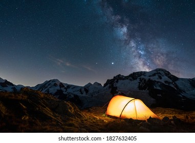 Red tent in the mountains under the night sky and the milky way.