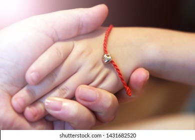 Red Thread With A Heart Of Gold On The Child's Hand So Close