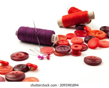 Red Threads And Buttons Lie On A White Background Isolated. Items For Sewing In Red Are On A White Background. Red Buttons, Pins And Thread On A White Background