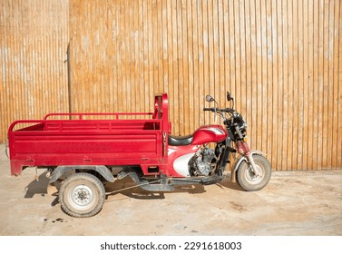 A red three-wheeled cargo motorcycle for transportation of summer works in the garden and park. Mowing grass on the lawn and cleaning areas. Tricycle - motorcycle - Tuk tuk