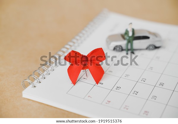 red thumbtack with ribbon\
marked on 1st of month on white calendar with blurred miniature\
business man and small car on grunge brown paper, new car, goal,\
due date concept