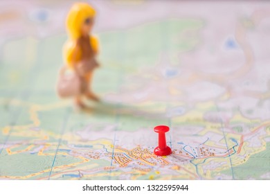 A red thumbtack is stuck in a tourist map next to a doll girl. Selective focus. . Geographical concept of vacation and travel