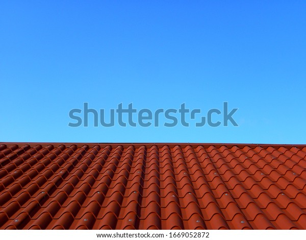 Red tile roof under blue sky. The photo is divided\
in half. One part is a roof made of clay tiles and the other is a\
pure blue sky.