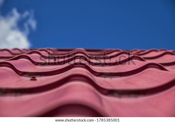 Red tile roof under blue sky. The photo is divided\
in half. One part is a roof made of clay tiles and the other is a\
pure blue sky.