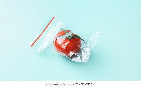 Red Tomato In A Zip Bag On A Green Background, The Concept Of Excess Food Packaging