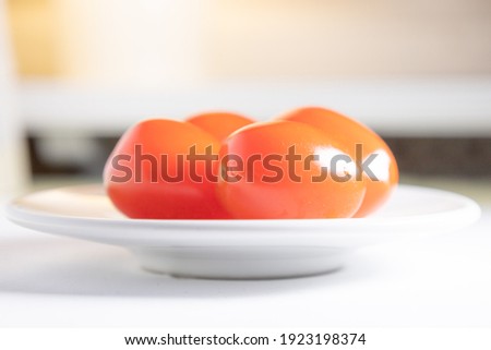 Red tomatoes laying on a white plate. Sideshot.
