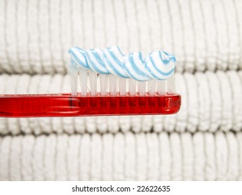 A red toothbrush full of toothpaste with white towels as background.