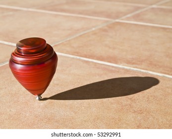 Red Top Spinning On Its Axis, With The Sun Casting Its Shadow On The Pavement