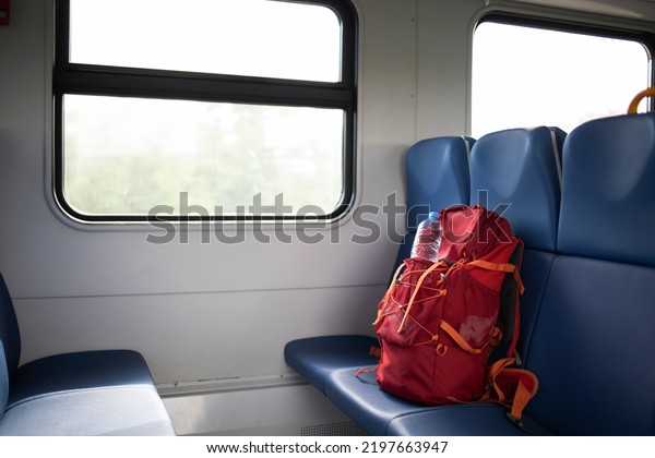 Red tourist backpack with a bottle of water in an\
electric train car. Without people. Travel by train. Concept:\
travel, weekend, vacation. Backpack, tourist backpack on the bench\
in the train 